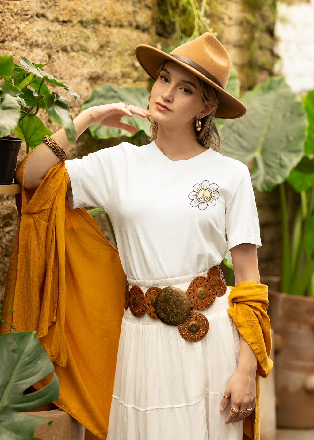Woman wearing a white t-shirt with a flower design, mustard cardigan, and brown hat in an outdoor setting.
