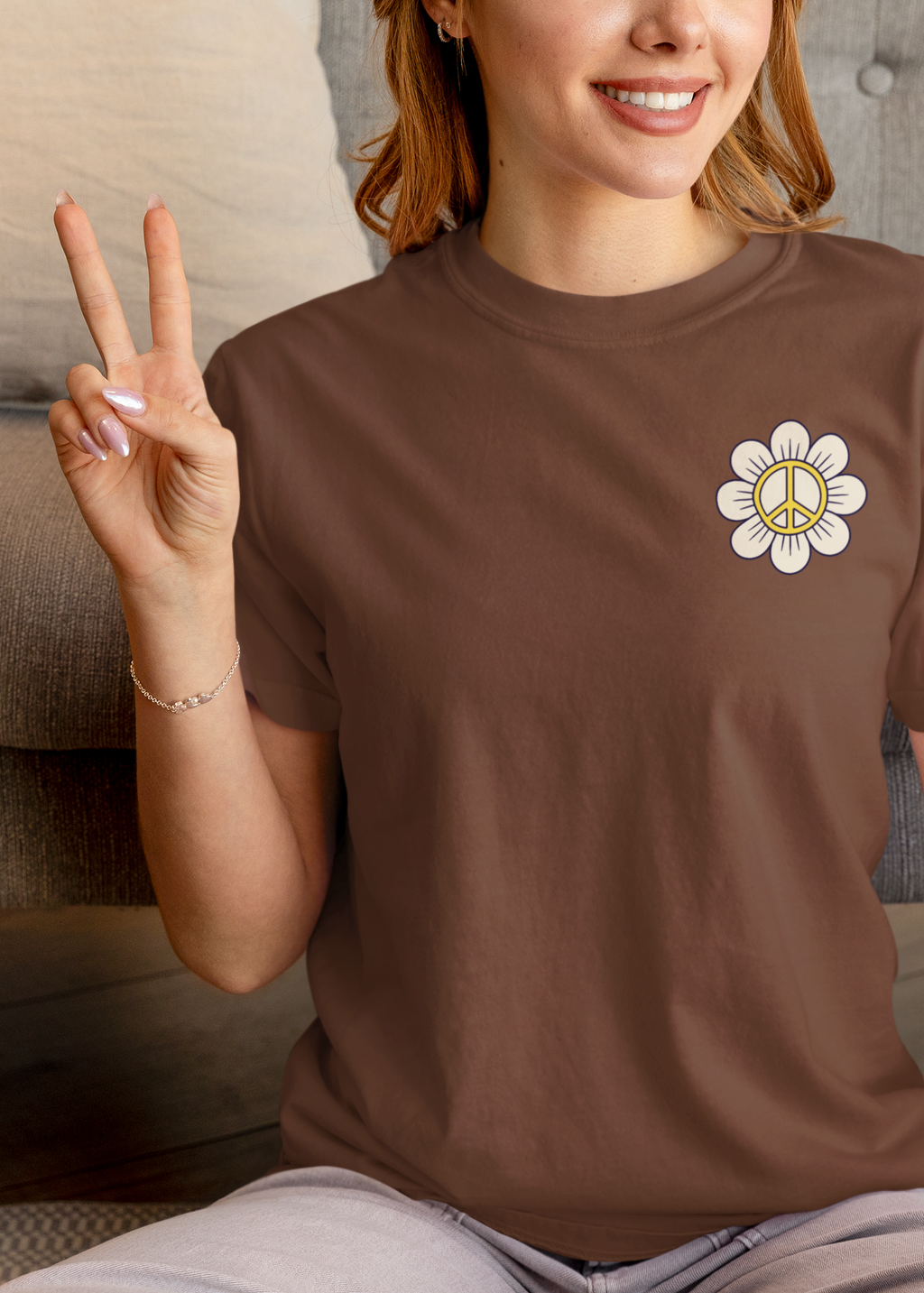 Person wearing a brown t-shirt with a peace symbol design, sitting on a couch.  Inspired by the scripture Philippians 4:7. 