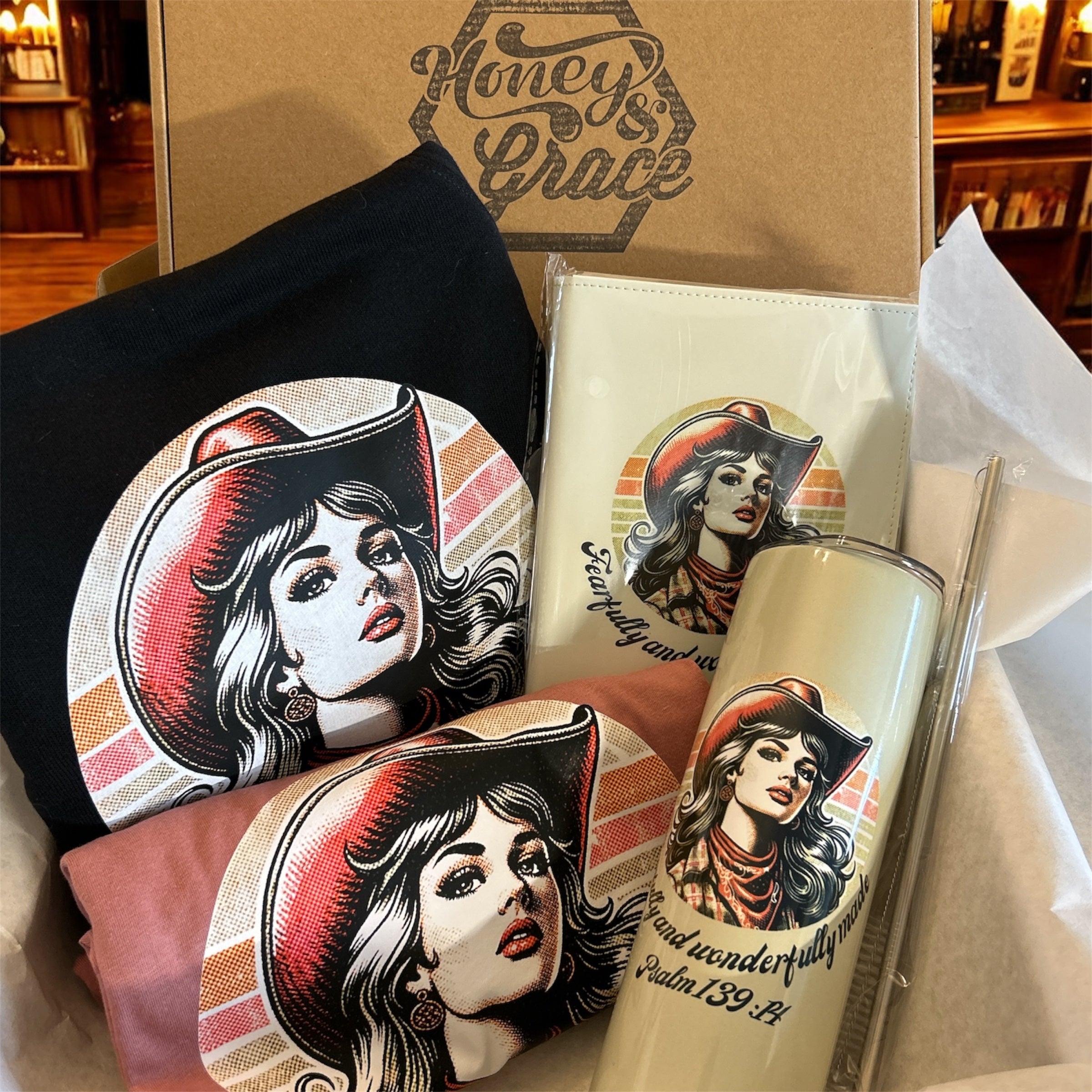 Product set with tumbler, sweater, tee, journal, and 'Honey & Grace' branded box.