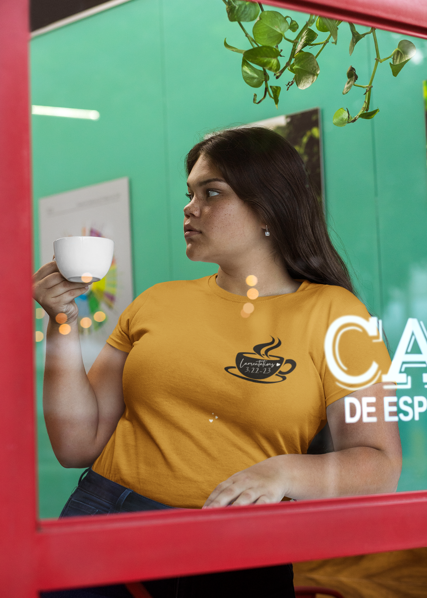 Woman in a mustard yellow shirt holding a cup, standing inside a vehicle with a green wall and red frame.