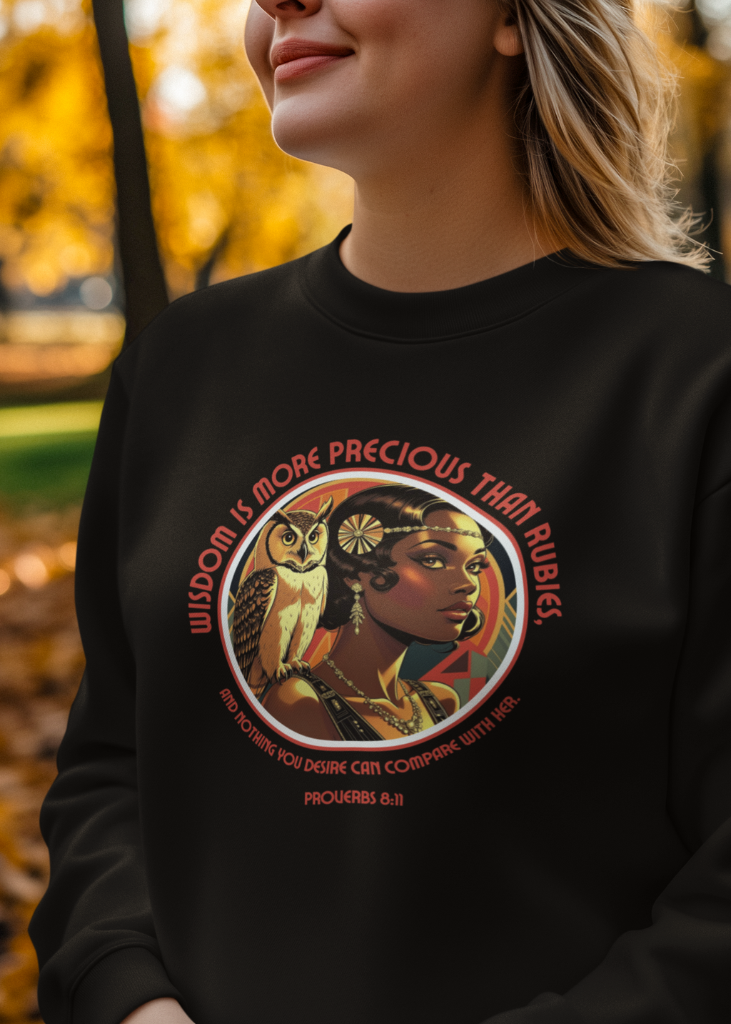 Person wearing a black sweatshirt with a Flapper graphic design featuring an owl and a 20s flapper with a scripture, set against a blurred autumn background.