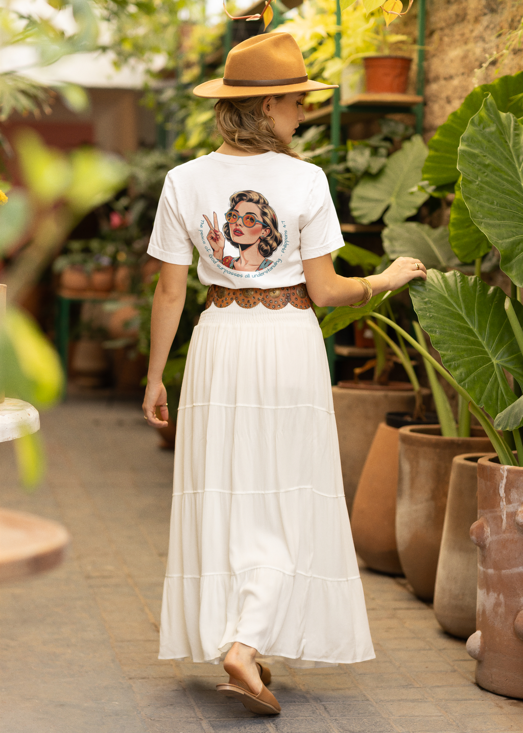 Woman in a garden wearing a white t-shirt with a graphic design and a white skirt.