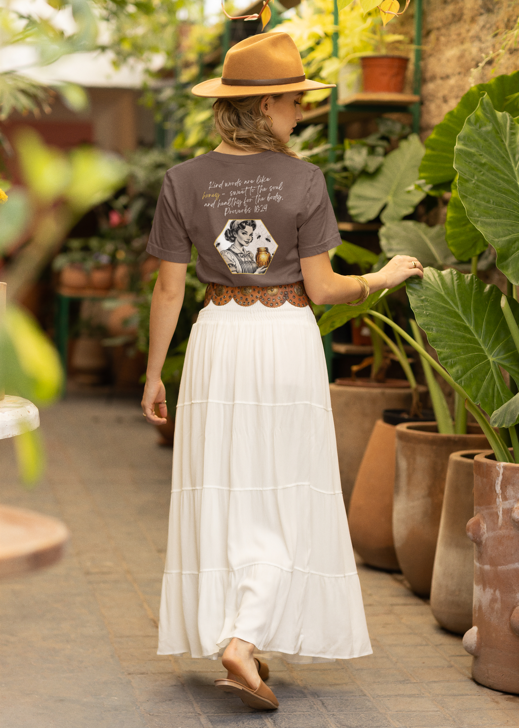 Woman in a garden wearing a brown hat, graphic t-shirt, and white skirt.