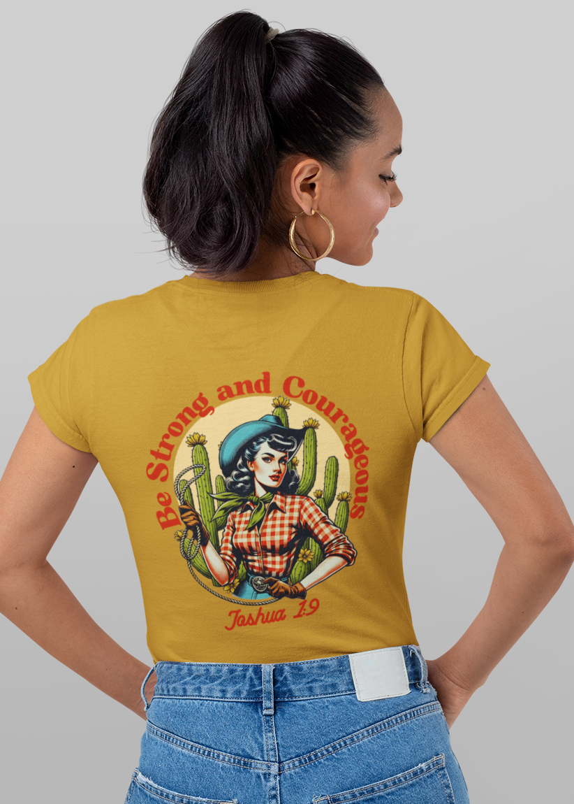 A woman modeling a mustard yellow short-sleeve t-shirt, shown from both the front and back against a light gray studio background. The front features a small circular graphic on the left chest, and the back features a large graphic of a woman in a cowboy hat surrounded by cacti with the text 'Be Strong and Good'.