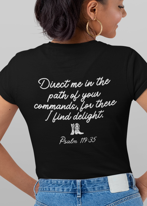 A woman modeling a black graphic T-shirt shown from both front and back against a light gray studio background. The front has white text reading 'Psalm 119:35' above a small illustrated scene, while the back has larger white script text and a small white cross graphic.