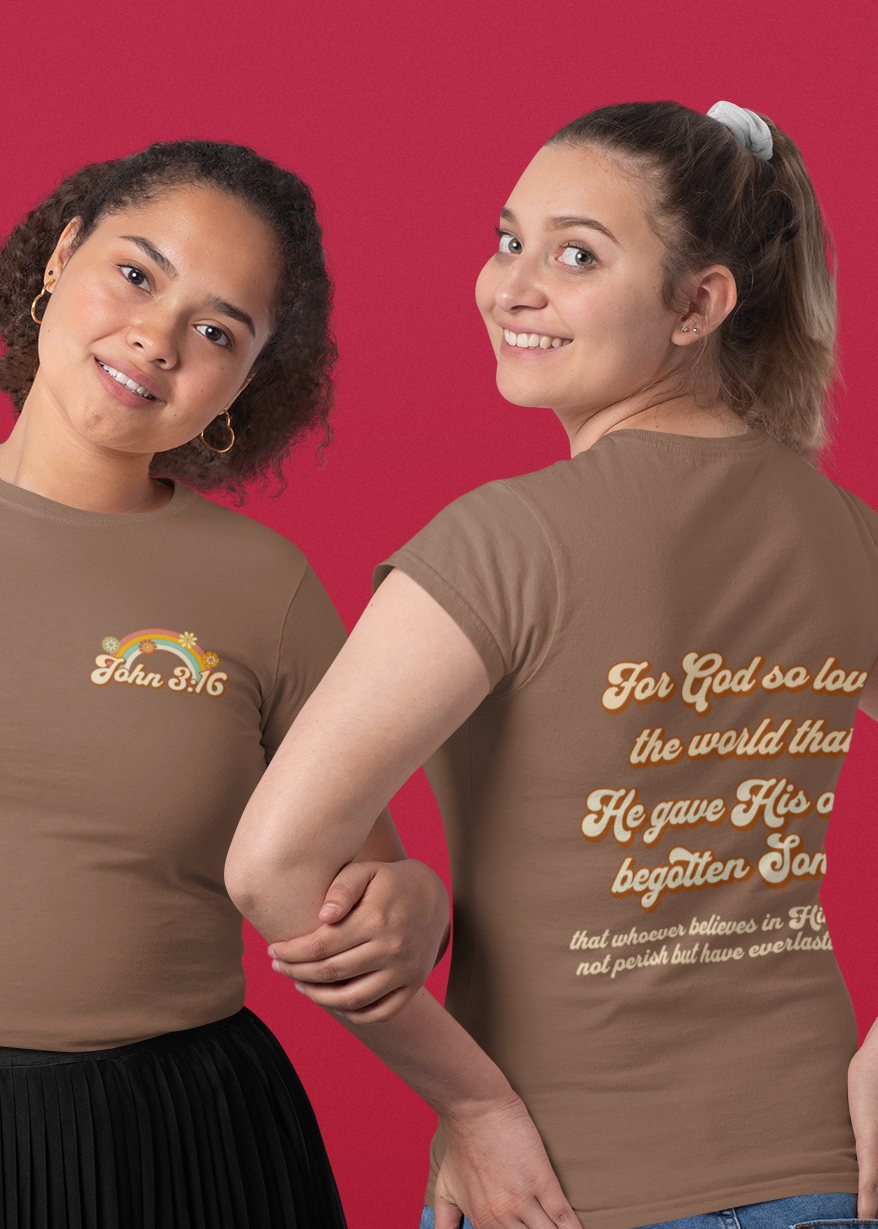 Two women modeling brown t-shirts with gold text and graphics against a solid red background. One shows the front of the shirt with a small gold logo, and the other shows the back with a large gold Bible verse.