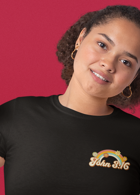 Two women modeling black t-shirts with gold text and graphics against a solid red background. The front view shows a gold rainbow and 'Flaws & Guts' text, while the back view shows a gold Bible verse.