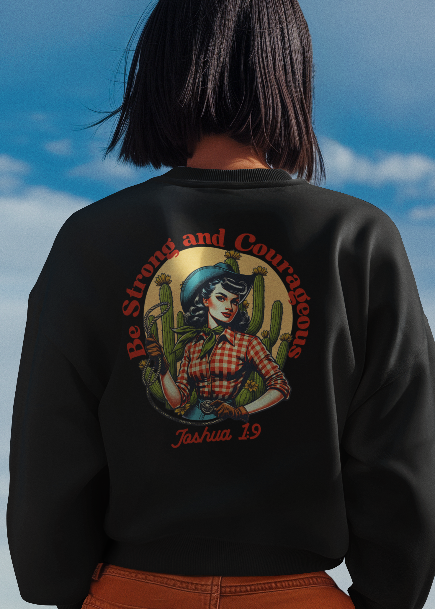 A person viewed from behind wearing a black crewneck sweatshirt with a large graphic print on the back, paired with orange-brown pants, set against a blue sky background.